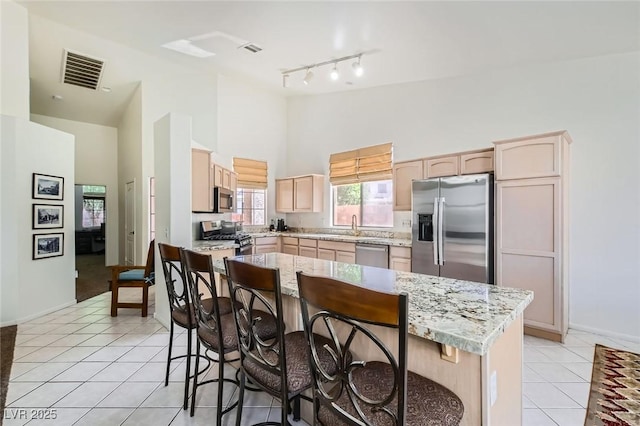 7515 Splashing Rock Dr, Las Vegas, NV 89131 - kitchen featuring appliances with stainless steel finishes, high vaulted ceiling, light brown cabinetry, a kitchen breakfast bar, and light tile patterned flooring