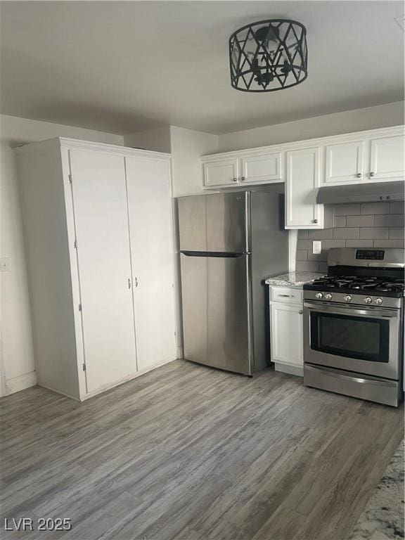 5280 Shreve Ave, Las Vegas, NV 89156 - kitchen featuring appliances with stainless steel finishes, under cabinet range hood, white cabinetry, wood finished floors, and decorative backsplash