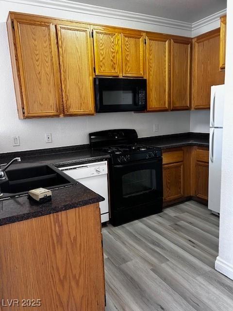 4730 E Craig Rd Unit 1148, Las Vegas, NV 89115 - kitchen with black appliances, brown cabinetry, dark countertops, crown molding, and light wood-type flooring