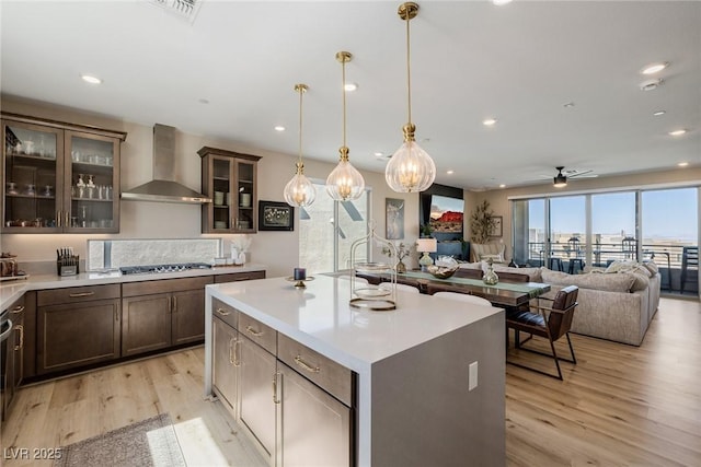 2151 Noble Perch St, Las Vegas, NV 89138 - kitchen featuring wall chimney range hood, light wood finished floors, ceiling fan, dark brown cabinets, and light countertops
