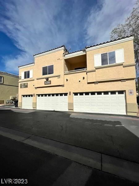 6316 Beige Bluff St Unit 201, North Las Vegas, NV 89081 - view of property with an attached garage, stucco siding, a tile roof, and driveway