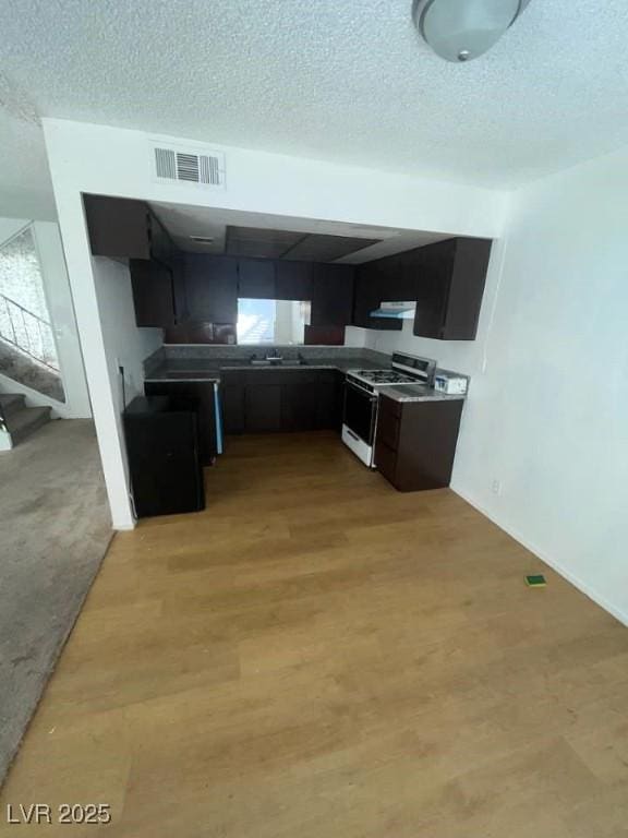4363 Spencer St Unit 8, Las Vegas, NV 89119 - kitchen with range with gas stovetop, a textured ceiling, light wood-style flooring, dark cabinetry, and under cabinet range hood