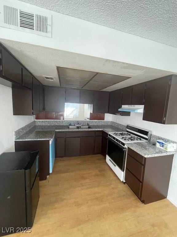 4363 Spencer St Unit 8, Las Vegas, NV 89119 - kitchen featuring gas range gas stove, under cabinet range hood, light wood-style flooring, a sink, and dark stone countertops