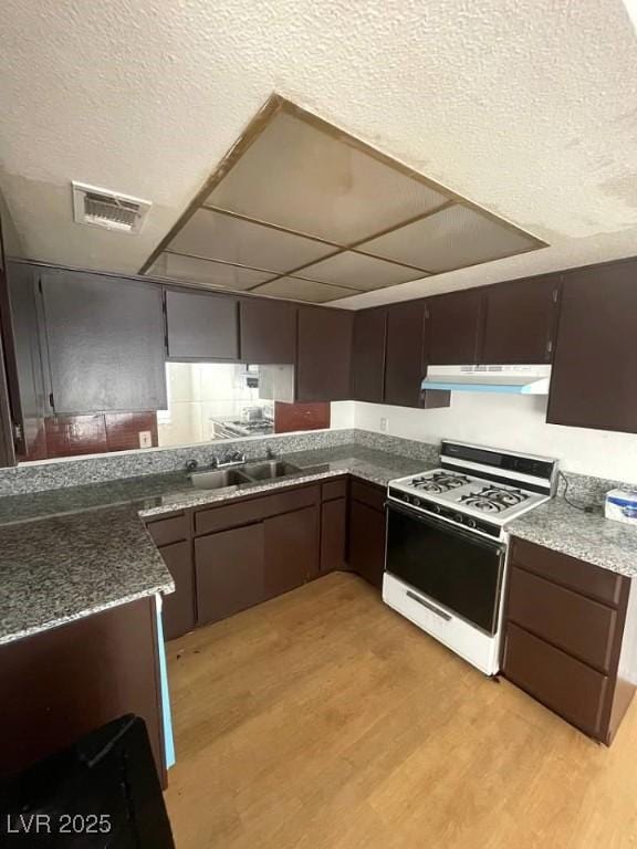 4363 Spencer St Unit 8, Las Vegas, NV 89119 - kitchen featuring white range with gas stovetop, a sink, light wood-type flooring, under cabinet range hood, and a textured ceiling