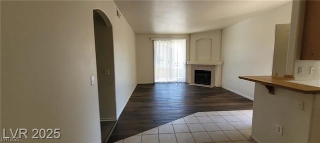 75 N Valle Verde Dr Unit 2121, Henderson, NV 89074 - unfurnished living room with arched walkways, dark wood finished floors, a tiled fireplace, and baseboards