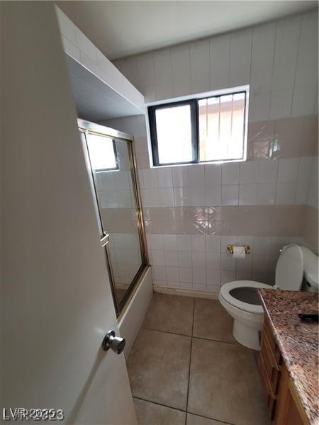 3480 E Hacienda Ave, Las Vegas, NV 89120 - full bathroom featuring toilet, tile patterned flooring, vanity, bath / shower combo with glass door, and tile walls