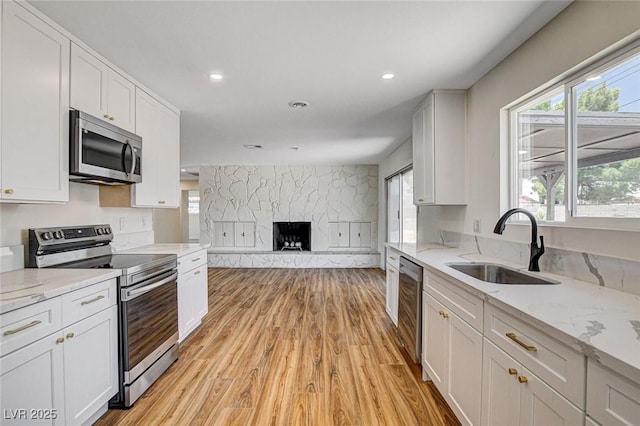 3386 El Camino Real, Las Vegas, NV 89121 - kitchen with stainless steel appliances, light wood-style flooring, a sink, white cabinetry, and a stone fireplace