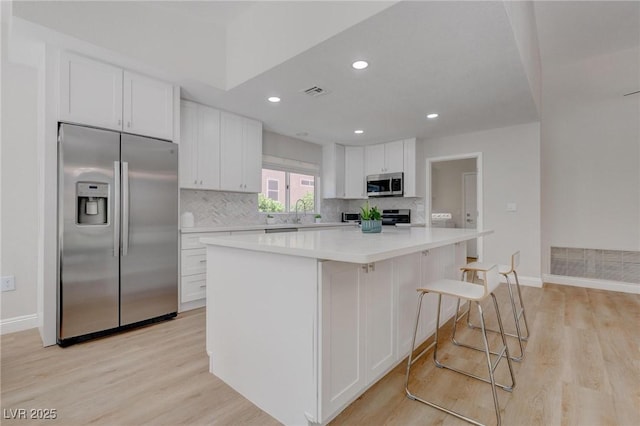 3040 Hidden Treasure Dr, Las Vegas, NV 89134 - kitchen with stainless steel appliances, white cabinets, light wood-style flooring, decorative backsplash, and light countertops
