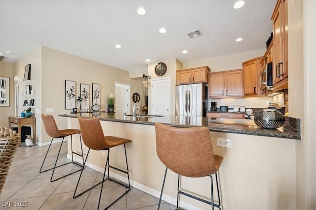 2453 Vivid Sky Pl, Henderson, NV 89044 - kitchen with stainless steel appliances, dark stone countertops, a kitchen bar, light tile patterned floors, and recessed lighting