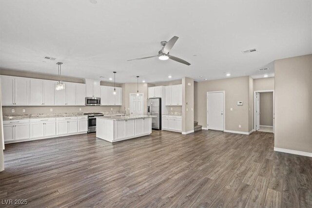 7051 Denio Island St, North Las Vegas, NV 89084 - kitchen with stainless steel appliances, open floor plan, white cabinetry, dark wood finished floors, and an island with sink