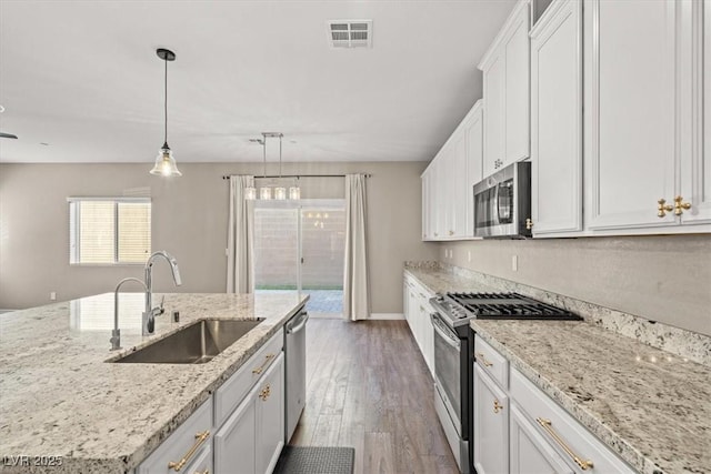 7051 Denio Island St, North Las Vegas, NV 89084 - kitchen with stainless steel appliances, a sink, wood finished floors, white cabinets, and light stone countertops