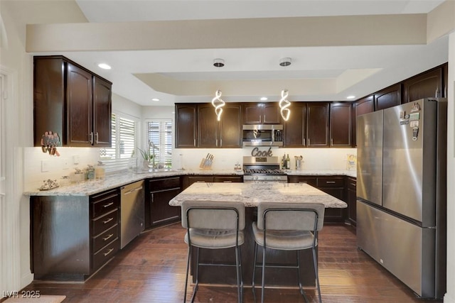 8224 Fawn Meadow Ave, Las Vegas, NV 89149 - kitchen with stainless steel appliances, dark brown cabinetry, dark wood-style flooring, light stone countertops, and a kitchen island