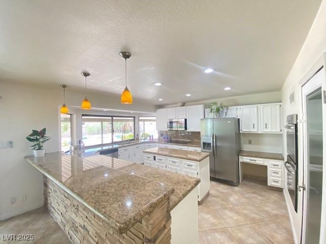 6315 Eldora Ave, Las Vegas, NV 89146 - kitchen with appliances with stainless steel finishes, a peninsula, white cabinetry, a kitchen island, and light stone countertops