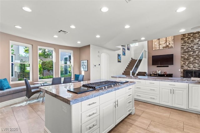 9301 Queen Charlotte Dr, Las Vegas, NV 89145 - kitchen featuring open floor plan, a center island, stainless steel gas cooktop, white cabinetry, and arched walkways