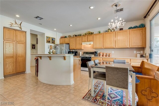 10361 Profeta Ct, Las Vegas, NV 89135 - kitchen featuring gas range, freestanding refrigerator, under cabinet range hood, light tile patterned floors, and light countertops