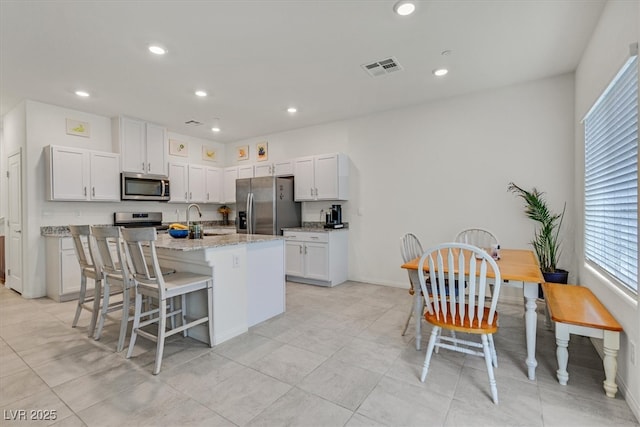 392 Canary Song Dr, Henderson, NV 89011 - kitchen featuring appliances with stainless steel finishes, a kitchen island with sink, light stone counters, a kitchen breakfast bar, and baseboards