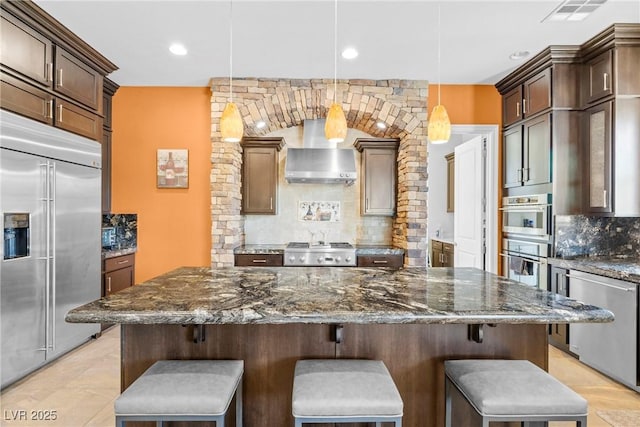 7504 Frittata Ave, Las Vegas, NV 89113 - kitchen with stainless steel appliances, tasteful backsplash, wall chimney range hood, a breakfast bar area, and dark stone countertops
