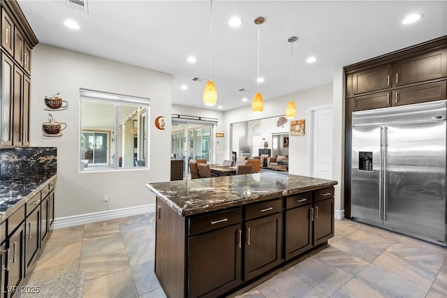 7504 Frittata Ave, Las Vegas, NV 89113 - kitchen with stainless steel built in fridge, dark stone countertops, dark brown cabinetry, baseboards, and a kitchen island