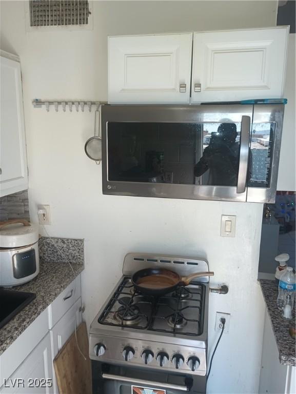 2409 Maroney Ave, Las Vegas, NV 89104 - kitchen view of gas range oven, stainless steel microwave, white cabinets, and dark stone counters