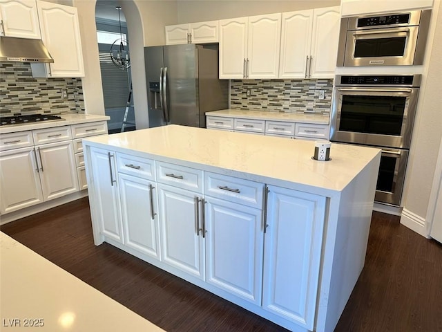 8931 Lansberry Ct, Las Vegas, NV 89147 - kitchen featuring appliances with stainless steel finishes, under cabinet range hood, dark wood-style flooring, tasteful backsplash, and white cabinetry
