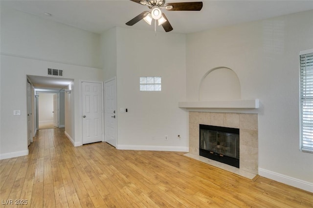 2251 Wigwam Pkwy Unit 824, Henderson, NV 89074 - unfurnished living room featuring a ceiling fan, a tiled fireplace, light wood-type flooring, baseboards, and a towering ceiling