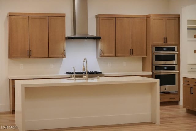 182 Robledo St, Las Vegas, NV 89138 - kitchen featuring wall chimney range hood, appliances with stainless steel finishes, light wood finished floors, light countertops, and a kitchen island with sink