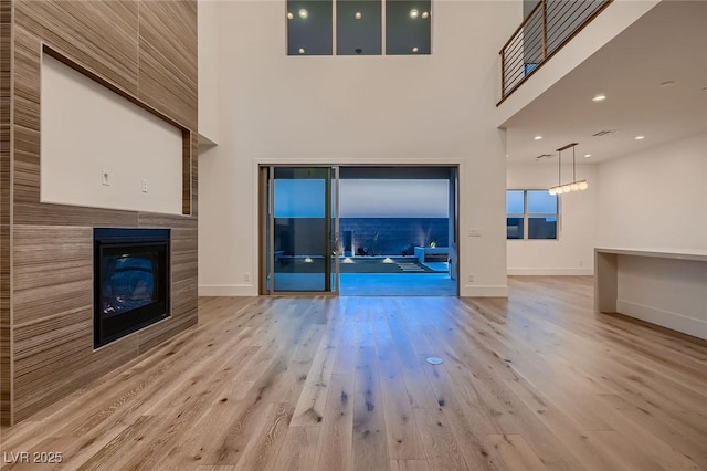 182 Robledo St, Las Vegas, NV 89138 - unfurnished living room featuring light wood-type flooring, a high ceiling, baseboards, and a tile fireplace