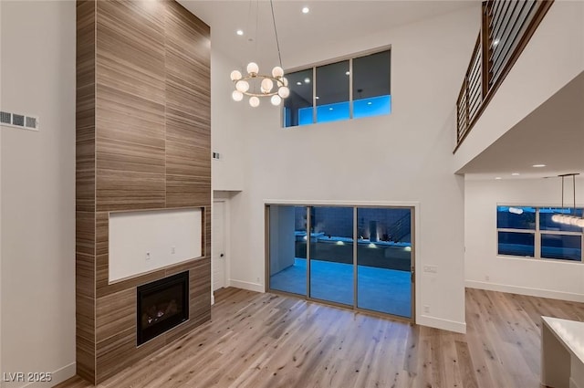 182 Robledo St, Las Vegas, NV 89138 - unfurnished living room with a towering ceiling, wood finished floors, a tile fireplace, baseboards, and a chandelier