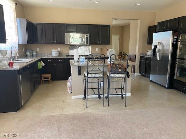 152 Lotus Vale Ave, Las Vegas, NV 89123 - kitchen with appliances with stainless steel finishes, a sink, a kitchen bar, a kitchen island with sink, and light tile patterned flooring