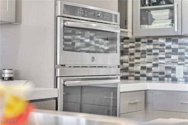 3111 Bel Air Dr Unit 22B, Las Vegas, NV 89109 - kitchen featuring stainless steel double oven, backsplash, gray cabinetry, and glass insert cabinets