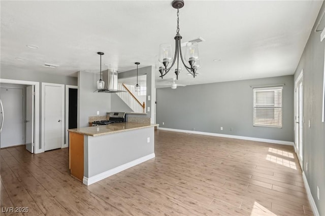 4552 Aviation St, Las Vegas, NV 89115 - kitchen with stainless steel range with gas stovetop, light wood-style flooring, wall chimney range hood, and a chandelier