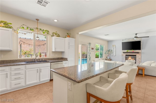 11226 Kenyan Sunshine Ct, Las Vegas, NV 89138 - kitchen featuring a sink, light tile patterned floors, a breakfast bar area, white cabinetry, and a fireplace