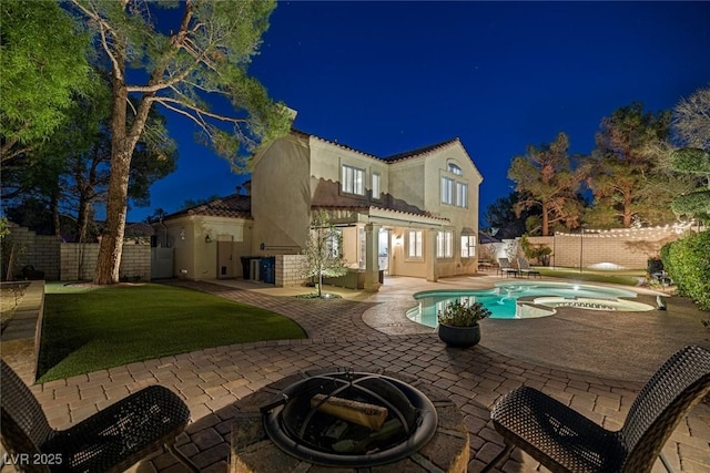 1921 Spyglass Dr, Henderson, NV 89074 - back of house at night with stucco siding, a fenced backyard, a patio area, and an in-ground hot tub