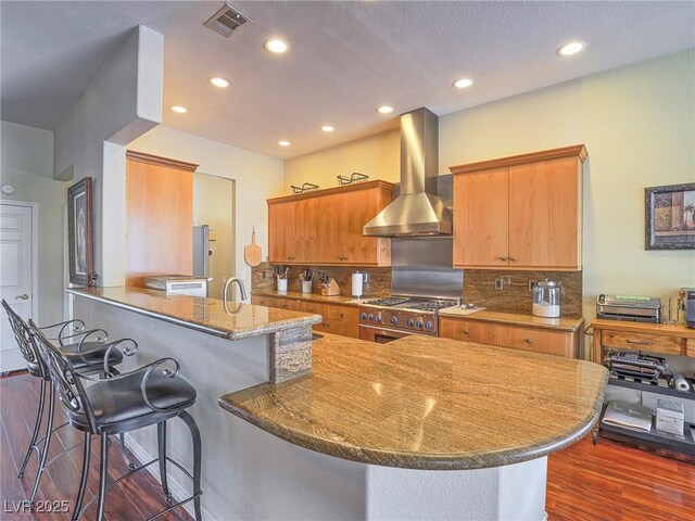 401 Obsidian St, Las Vegas, NV 89145 - kitchen featuring wall chimney exhaust hood, stainless steel stove, dark wood-style floors, a kitchen bar, and stone countertops