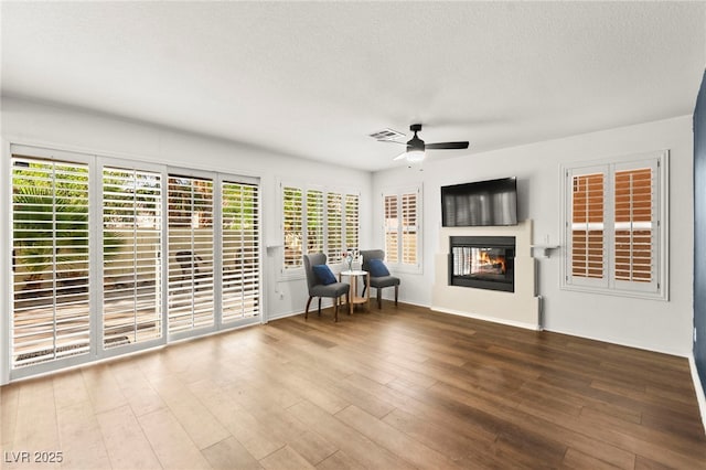 8612 Danza Del Sol Dr, Las Vegas, NV 89128 - living area featuring a glass covered fireplace, ceiling fan, wood finished floors, plenty of natural light, and a textured ceiling