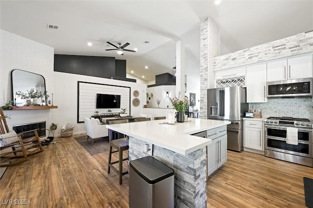 211 Kokopelli Ct, Henderson, NV 89074 - kitchen with appliances with stainless steel finishes, a ceiling fan, a fireplace, light countertops, and a kitchen breakfast bar