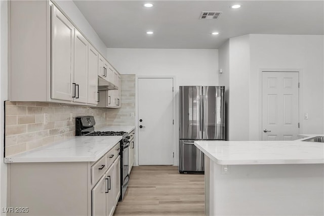 576 Foster Springs Rd, Las Vegas, NV 89148 - kitchen with freestanding refrigerator, range with gas cooktop, under cabinet range hood, light wood finished floors, and backsplash