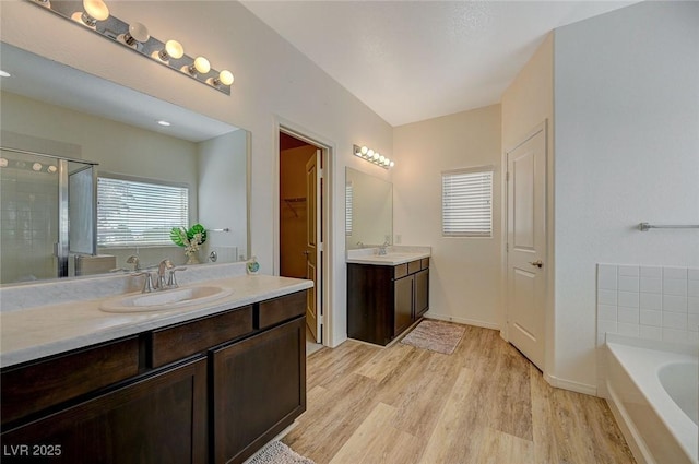 5244 Fiery Sky Ridge St, Las Vegas, NV 89148 - bathroom featuring two vanities, wood finished floors, a garden tub, a shower stall, and a walk in closet