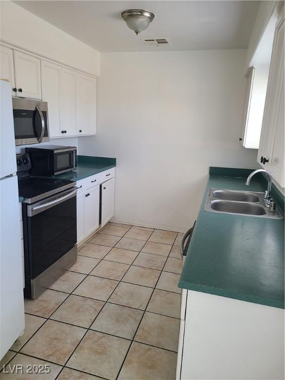 129 Maple St, Henderson, NV 89015 - kitchen featuring appliances with stainless steel finishes, a sink, white cabinets, light tile patterned flooring, and dark countertops
