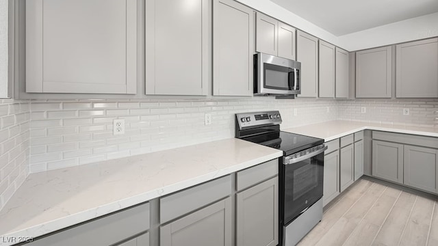 4450 E Brusca Ct, Pahrump, NV 89061 - kitchen with appliances with stainless steel finishes, gray cabinets, backsplash, light stone countertops, and light wood-type flooring