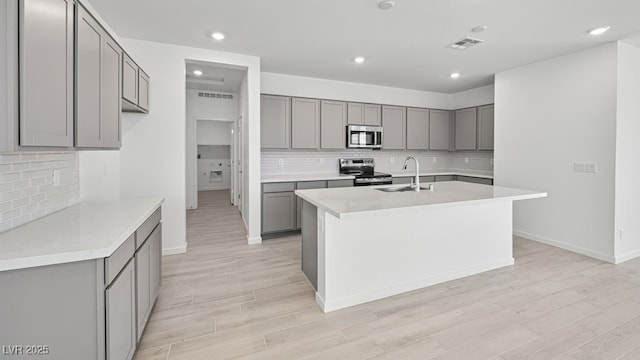 4450 E Brusca Ct, Pahrump, NV 89061 - kitchen featuring appliances with stainless steel finishes, gray cabinetry, tasteful backsplash, an island with sink, and light wood-type flooring