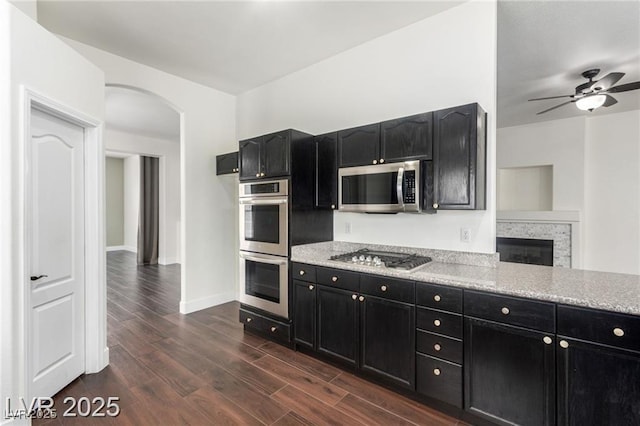 10058 Saint Augustine St, Las Vegas, NV 89183 - kitchen featuring appliances with stainless steel finishes, dark cabinets, arched walkways, a ceiling fan, and dark wood-style flooring