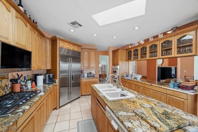 1105 Malachite Ct, Henderson, NV 89011 - kitchen featuring stainless steel appliances, a sink, a skylight, glass insert cabinets, and light tile patterned floors