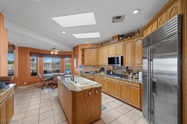 1105 Malachite Ct, Henderson, NV 89011 - kitchen featuring stainless steel appliances, a sink, a skylight, light tile patterned floors, and an island with sink