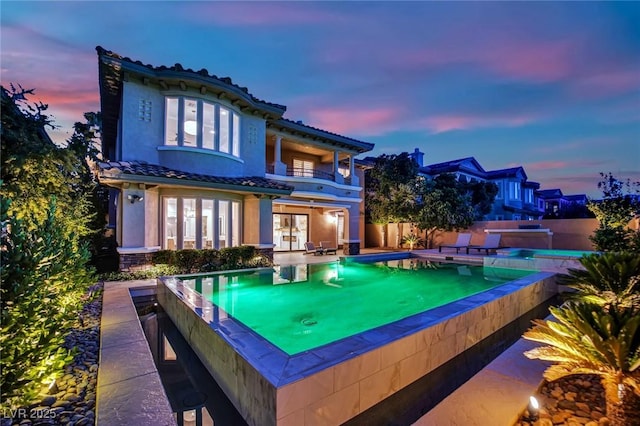 1972 Alcova Ridge Dr, Las Vegas, NV 89135 - back of property at dusk featuring a balcony, french doors, a tile roof, and an outdoor pool