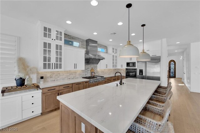 1972 Alcova Ridge Dr, Las Vegas, NV 89135 - kitchen featuring built in appliances, wall chimney range hood, a sink, backsplash, and a large island with sink