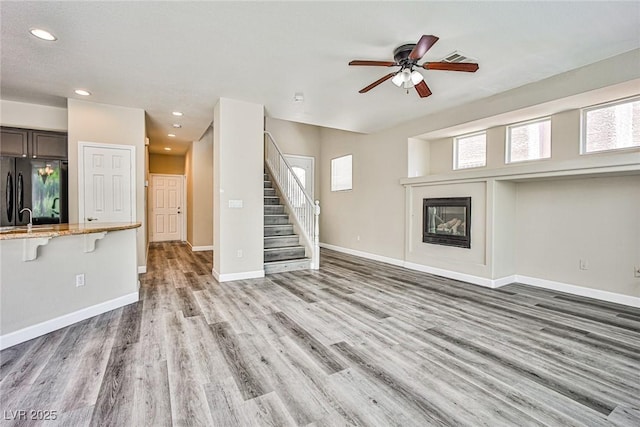 7083 Somera Way, Las Vegas, NV 89113 - unfurnished living room featuring light wood-style floors, a ceiling fan, stairway, baseboards, and a glass covered fireplace