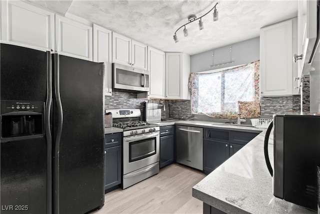 5004 Cannon Blvd, Las Vegas, NV 89108 - kitchen with stainless steel appliances, white cabinets, light wood-style floors, decorative backsplash, and light stone countertops