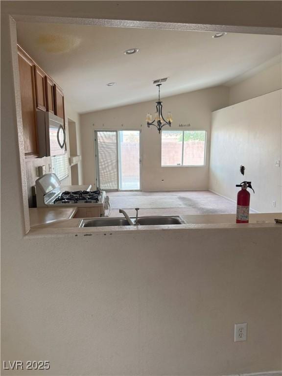 6642 Cinnabar Coast Ln, North Las Vegas, NV 89084 - kitchen with white range with gas cooktop, lofted ceiling, brown cabinets, hanging light fixtures, and a chandelier