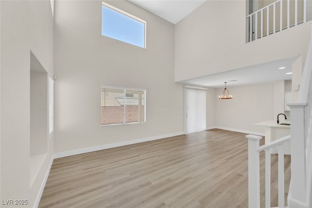 4132 Joyous St, North Las Vegas, NV 89032 - unfurnished living room with a high ceiling, a chandelier, light wood-style flooring, baseboards, and a sink